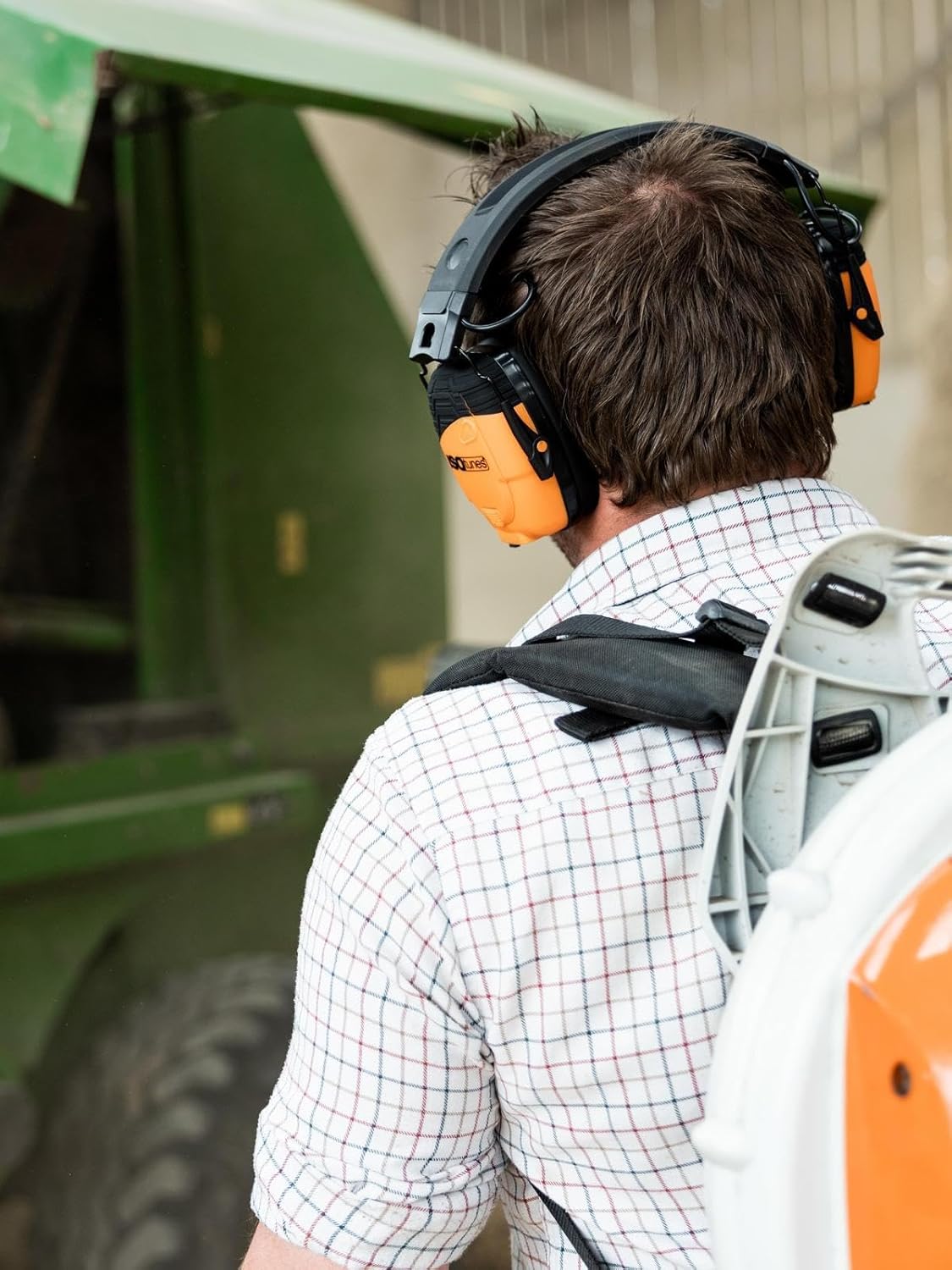 Man wearing ISOtunes LINK 2.0 ear defenders while carrying a backpack leaf blower beside a tractor
