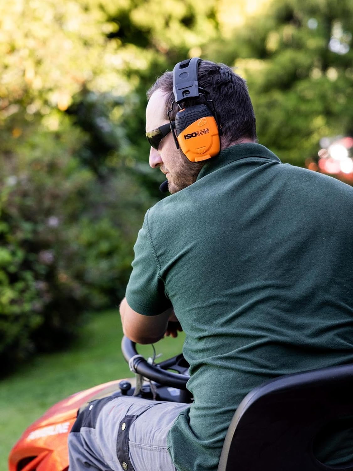 Man wearing ISOtunes LINK 2.0 Bluetooth ear defenders and sunglasses while driving a ride-on lawn mower